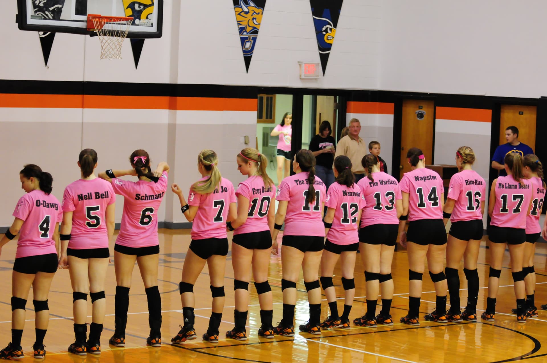 Greenville women's volleyball players lined up along the baseline in pink awareness jerseys.